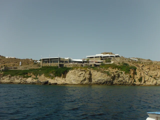 Stone buildings of Cavo Paradiso above a rocky shoreline, viewed from the sea