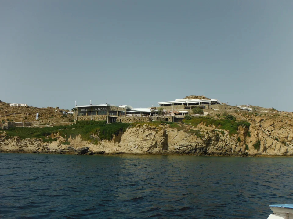 Stone buildings of Cavo Paradiso above a rocky shoreline, viewed from the sea