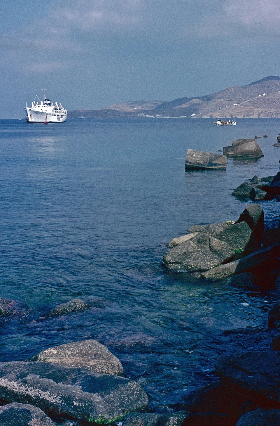 A white passenger ship and a small boat beyond the concrete blocks of a breakwater