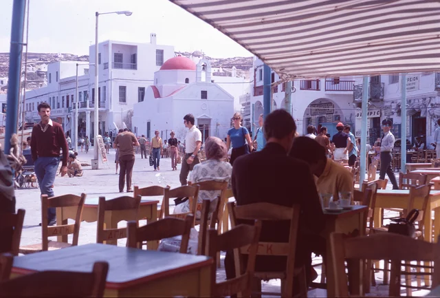 People seated at café tables under a striped awning beside a busy waterfront