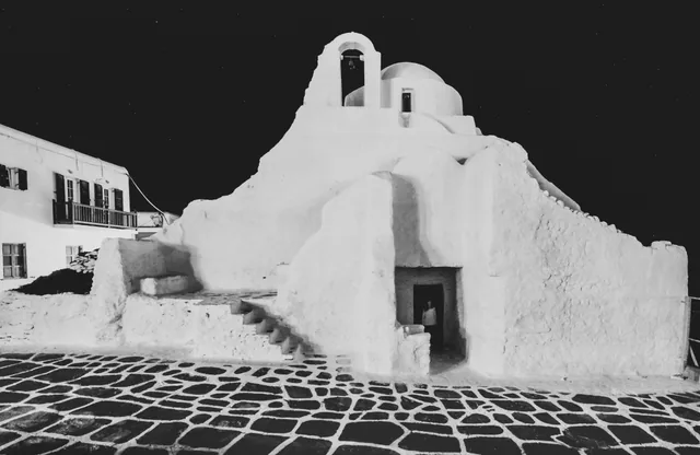 The whitewashed Panagia Paraportiani church illuminated against the night sky in Mykonos Town
