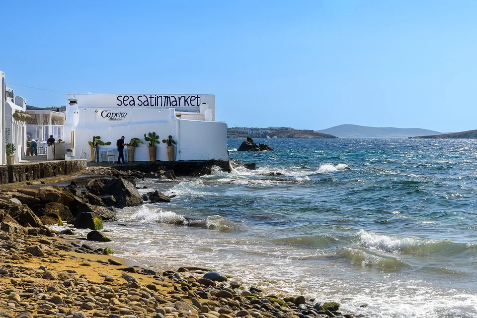 The signed Sea Satin Market exterior and rocky Mykonos waterfront in June 2024