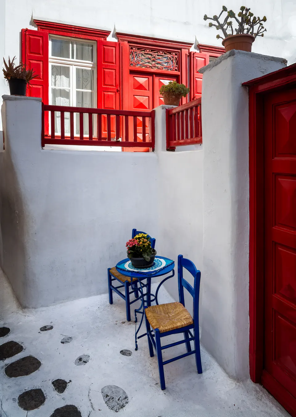 Red shutters and blue chairs against whitewashed Mykonos Town walls