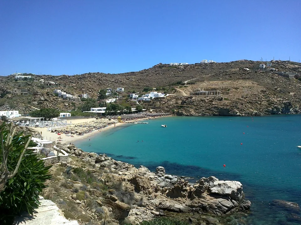 Super Paradise Beach seen across the bay, with sand, loungers and the surrounding rocky hillside